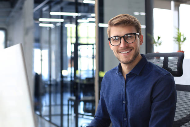 istock Good looking young business man looking at camera and smiling while sitting in the office. 1466263973
