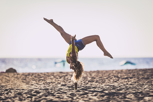 Young woman having fun while doing a handstand on the beach in summer day. Copy space.