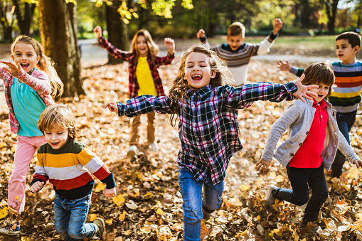 Group of happy kids having fun while running in autumn day with their arms outstretched at the park.
