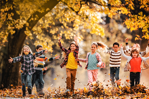 Playful children having fun while running in autumn day at the park.
