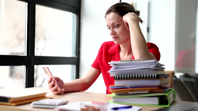 Thoughtful beautiful business woman is using phone at workplace