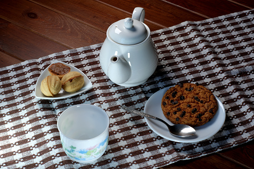 Teapot with a cup and sweet cookies on a brown napkin on a dark table close-up top view