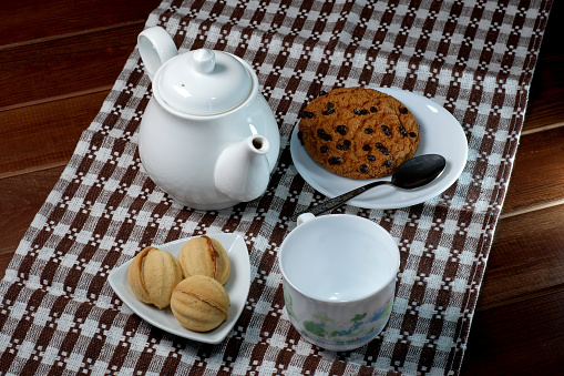 Teapot with a cup and sweet cookies on a brown napkin on a dark table close-up top view