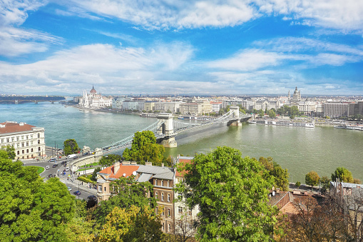 This captivating photo of Budapest's cityscape depicts a high-angle view during the daytime. The famous Chain Bridge dominates the foreground, elegantly spanning the Danube River. In the distance, the stunning Hungarian Parliament Building and towering St. Stephen's Basilica can be seen, showcasing the city's impressive architecture and rich history.  The photo showcases the seamless blend of old and new architecture that defines Budapest, with the classic landmarks and modern buildings beautifully juxtaposed against each other.