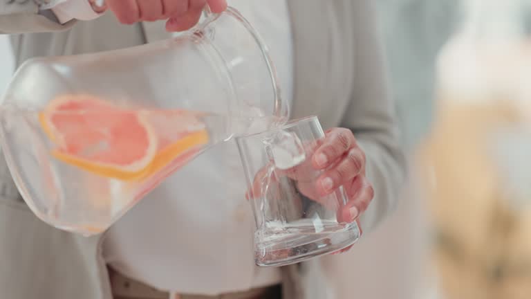 Hands, jug and glass for pouring water in home for health, wellness and citrus for detox nutrition. Woman, grapefruit drink and vitamin c for diet, healthcare and energy to start morning in house