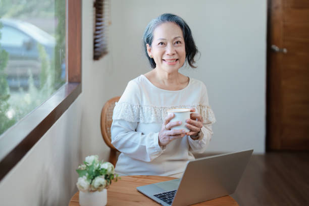 istock Portrait of an elderly Asian woman in modern pose doing computer work and drinking coffee. 1466290897