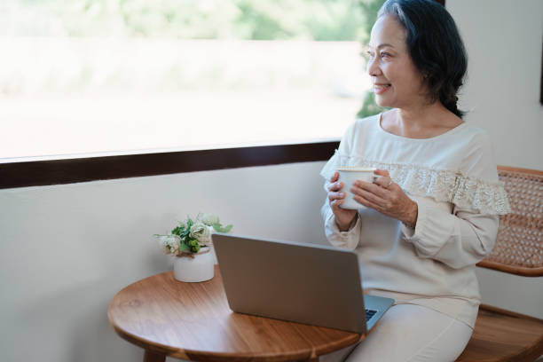 istock Portrait of an elderly Asian woman in modern pose doing computer work and drinking coffee. 1466290961
