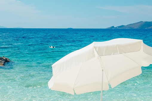 white sun umbrella clear blue water on background copy space