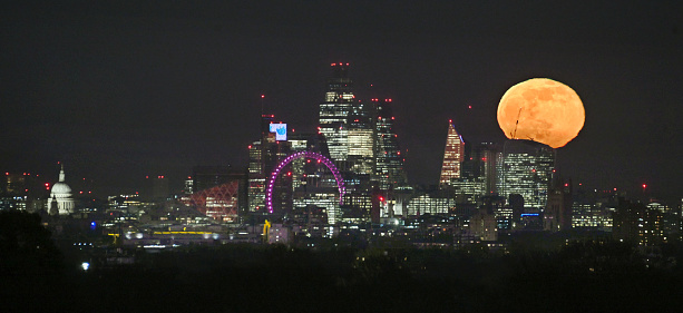 Full moon rising over the London cityscape.  From Richmond Park (eleven miles distance) the  perspective in a rare and spectacular phenomenon makes the moon look very large and red as it emerges just after sunset. No image manipulation