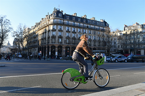 Paris, France-02 14 2023: Young woman riding a bicycle on a cycle path in Place de la Bastille in Paris, France.