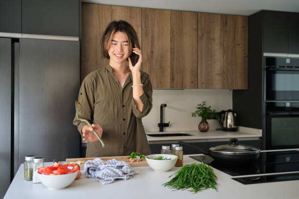 istock Asian young man talking by phone while cooking at kitchen. 1466296862