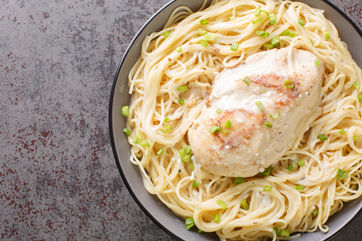 Tender chicken cooked in a creamy Italian flavored sauce and served on a bed of angel hair pasta closeup in the bowl on the table. Horizontal top view from above