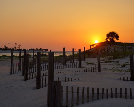 The bright sun in orange sunset sky shining over wooden fences on sandy Saint George Island, Florida