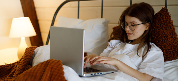 Young woman in bed with laptop, lazy leisure time at home.