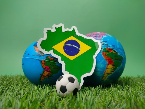 A ball and brazil flag sticker on a green field with a blurred globe behind it.