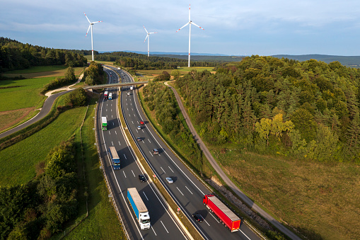 Rural, multiple lane highway with truck and car traffic at sunset, wind turbines in the background, aerial view.