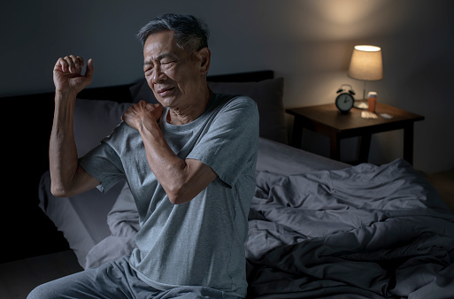 Insomnia senior Asian man suffering from neck and shoulder pain at night.