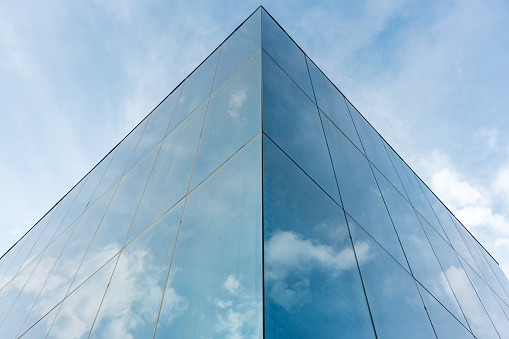 A low angle shot of a modern building with glass wall reflecting the cloudy blue sky