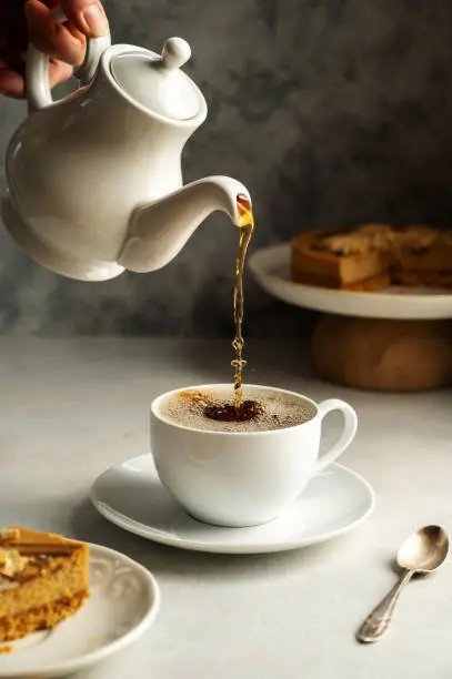 Photo of Pouring hot black tea in white, ceramic cup, served with cake