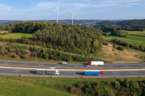 Truck traffic on rural highway, wind turbines in the background, aerial view.