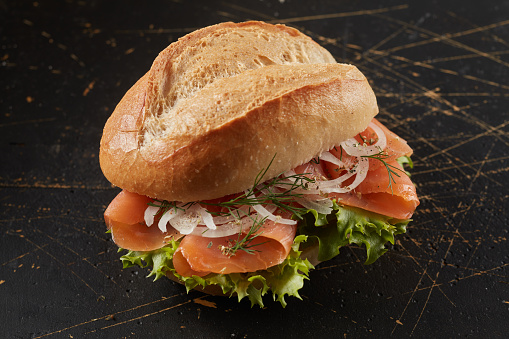 A closeup of a smoked salmon sandwich on a black wooden surface
