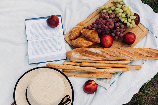 A still life with croissants, baguette, fresh fruits, summer hat and book