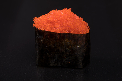 A closeup of tobiko, flying fish roe on a black background