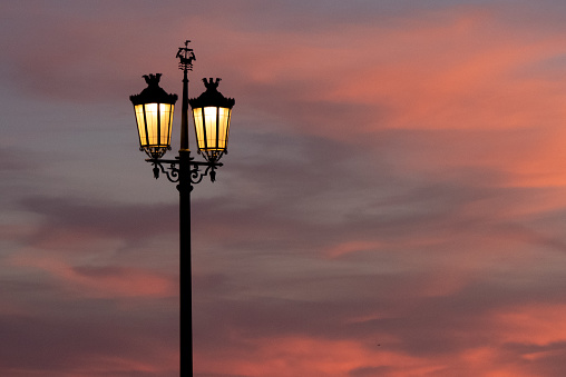 Street lamp with golden light during sunset with pink and purple clouds.