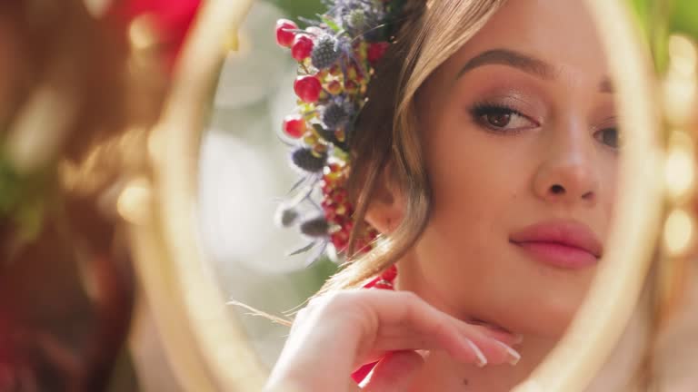 Beautiful bride dressed in ukrainian ethno clothes sitting on chair and look into the mirror. Woman trying on a necklace. Morning of the bride concept. Close up Reflection in the mirror