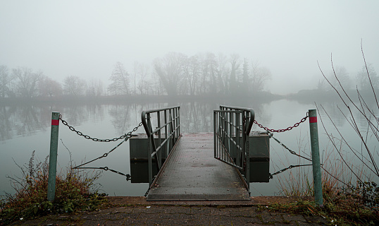 Image of a pier next to the river, the environment is mysterious and extremely foggy