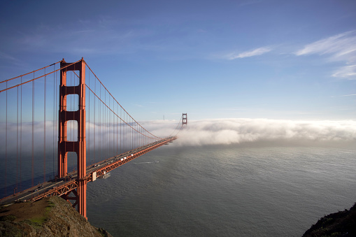 Dramatic photo of cars driving big red bridge above Pacific Ocean during spring cloudy morning with flowers in San Francisco city, the United States