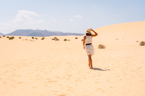 A young Caucasian female in a white light dress walking through the dunes of the Corralejo Natural Park, Fuerteventura, Canary Islands, Spain