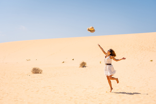 A young Caucasian female happily throwing her hat up in the dunes of the Corralejo Natural Park, Fuerteventura, Canary Islands, Spain