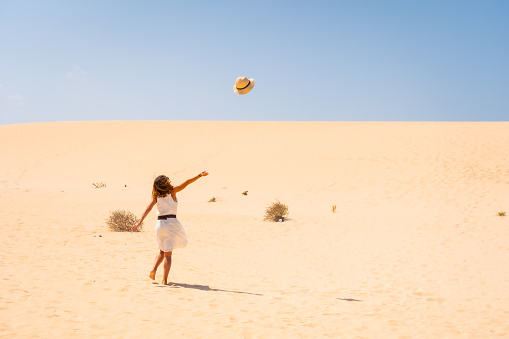 A young Caucasian female happily throwing her hat up in the dunes of the Corralejo Natural Park, Fuerteventura, Canary Islands, Spain