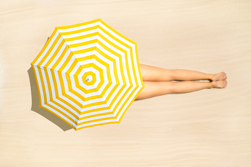Top view of woman in bikini lying and sunbathes under yellow umbrella on tropical Seychelles sand beach. Aerial, drone view