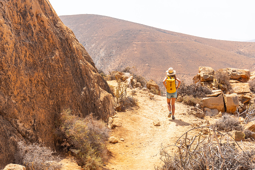 A girl hiker with a yellow backpack on the Mirador de la Penitas trail in the Penitas canyon, Fuerteventura, Canary Islands, Spain