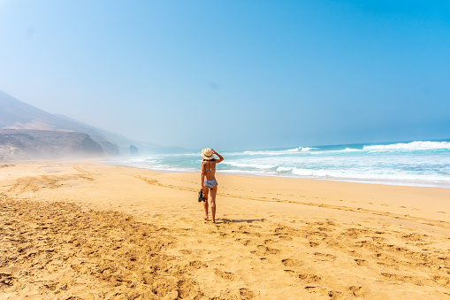 A back view of a young woman walking alone on the wild Cofete beach of the Jandia natural park, Spain