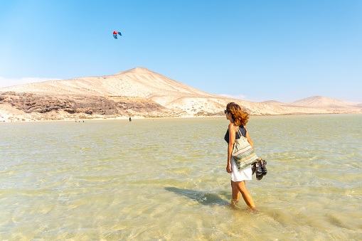 A young Spanish woman walking through the crystal clear water on Sotavento beach, Fuerteventura, Spain