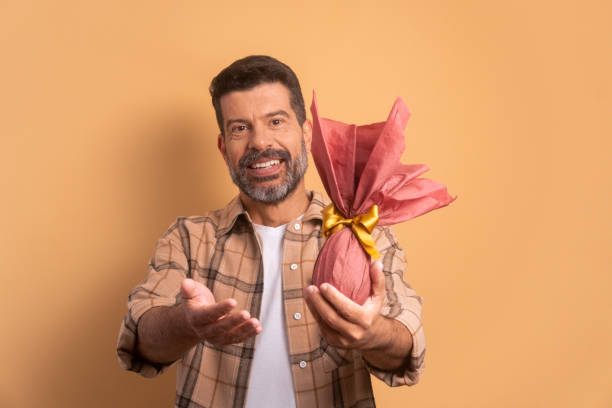 istock cheerful caucasian man offering easter egg in beige studio background. holiday, easter, celebration concept. 1466336424