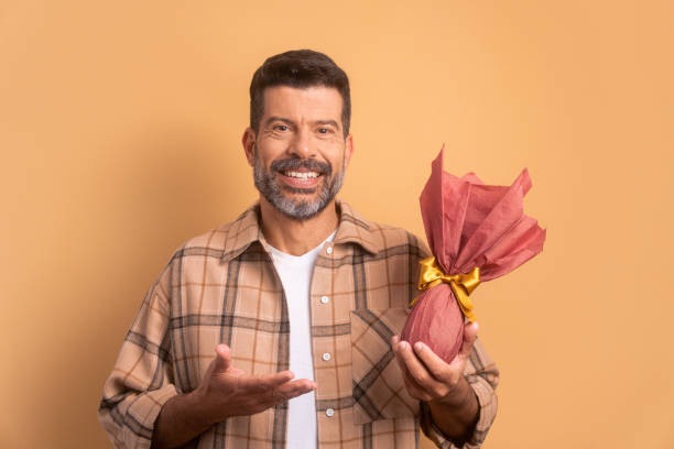 joyful brazilian man offering easter egg in beige colors. holiday, easter, celebration concept.