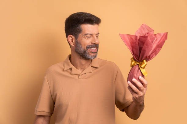 istock cheerful mature man looking at easter egg in all beige colors. holiday, easter, celebration concept. 1466336457