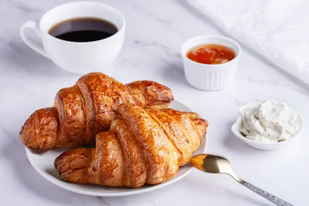 Photo of Fresh sweet croissants with cottage cheese and apricot jam for breakfast. Continental breakfast on a white table