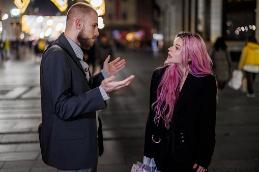 Photo of a young modern couple walking in the street during the night and having a discussion about relationship problems.