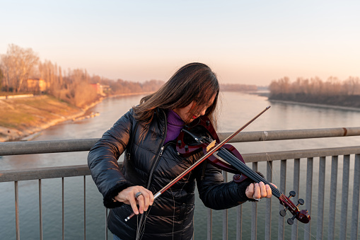 attractive middle aged woman playing an electric violin outdoors over an iron bridge