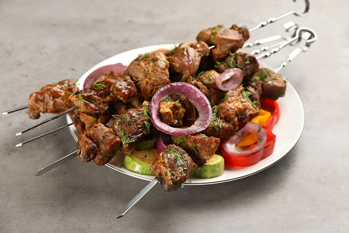 Metal skewers with delicious meat and vegetables served on light grey table