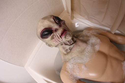 A very spooky alien is relaxing in the bathtub. He has a fit torso and lays down in the water.