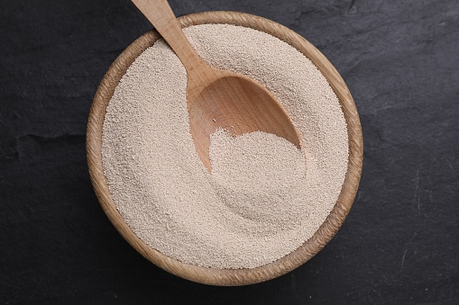 Bowl and spoon with active dry yeast on black table, top view