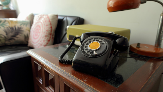 There is a black antique dial telephone on the table next to the sofa