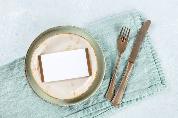 istock Dinner invitation. A card on a plate, with silverware and a teal textile napkin 1466352102