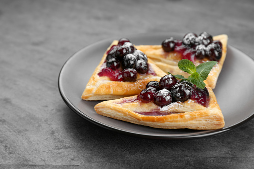 Fresh tasty puff pastry with sugar powder, jam, sweet berries and mint on grey table, closeup